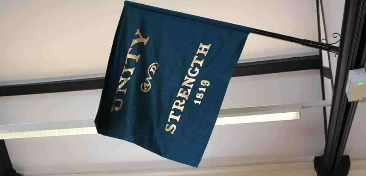 Flag with the words Unity and Strength hanging from a wall mounted pole.