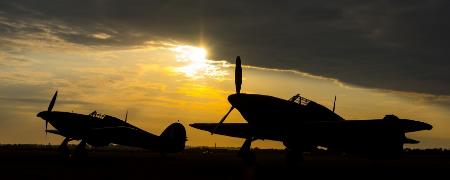 2 Hawker Hurricanes parked in a field at dusk.