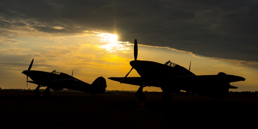 2 Hurricane fighter planes parked in a field at sunset.