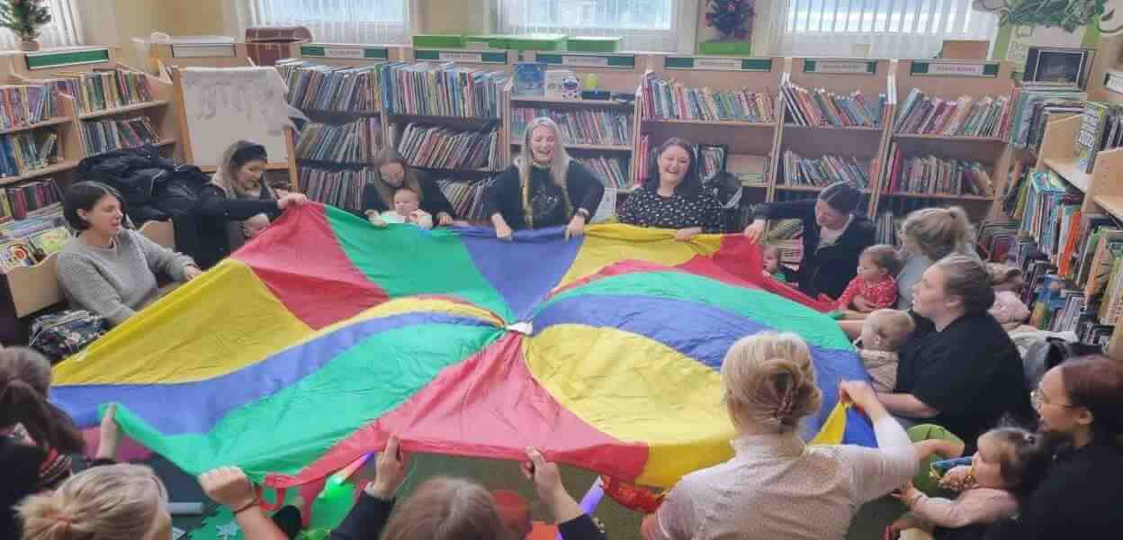 Bookstart Baby session with children and parents holding a multicoloured parachute.