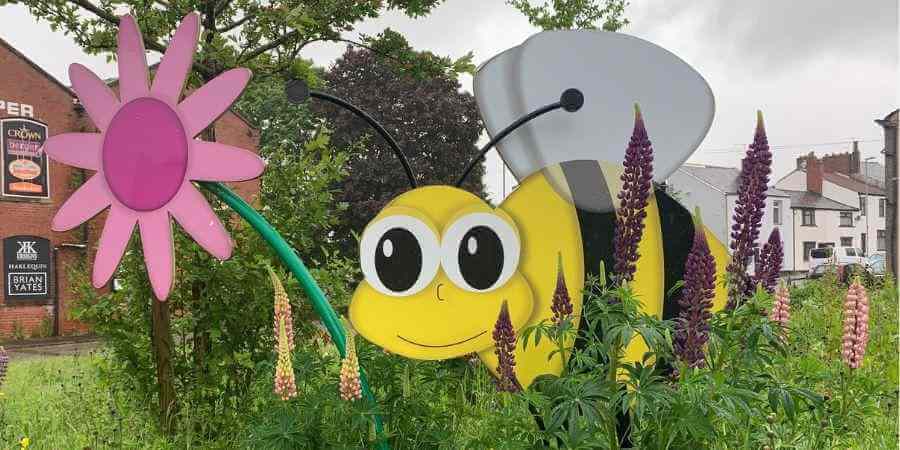 Large bee sign in a grass verge, indicating the area is a nature friendly zone.