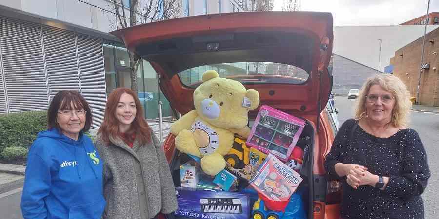 Kathryn and Ruth from Rochdale Musical Theatre Company stood with Helen Walton outside Number One Riverside in front of a car boot full of donated toys.