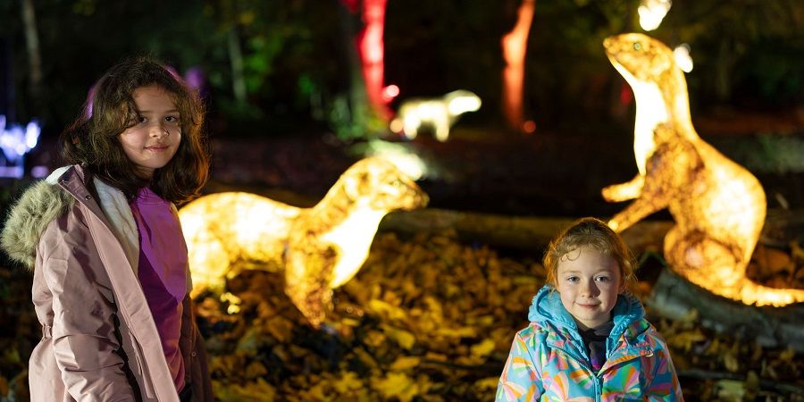 2 children in front of 2 illuminated stoat sculptures.