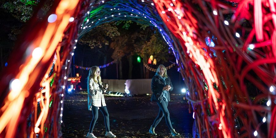 2 people walking past a lit up sculpture.