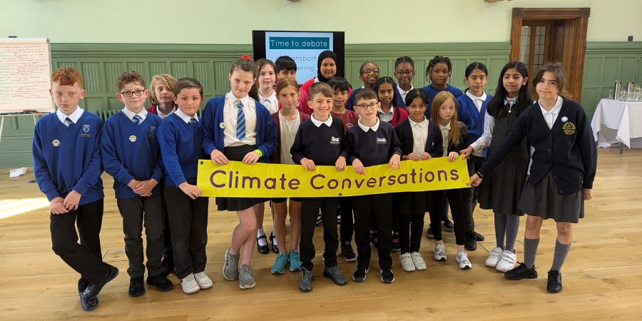 School children holding up a yellow banner that says 'Climate Conversations'