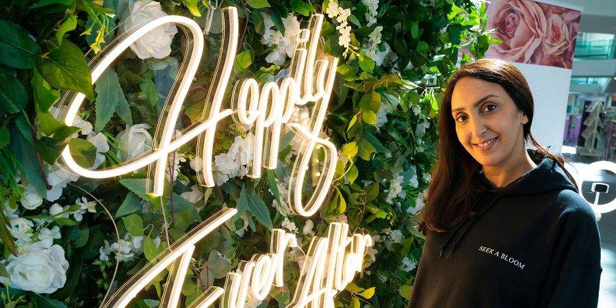 A woman standing in front of an illuminated flower wall.