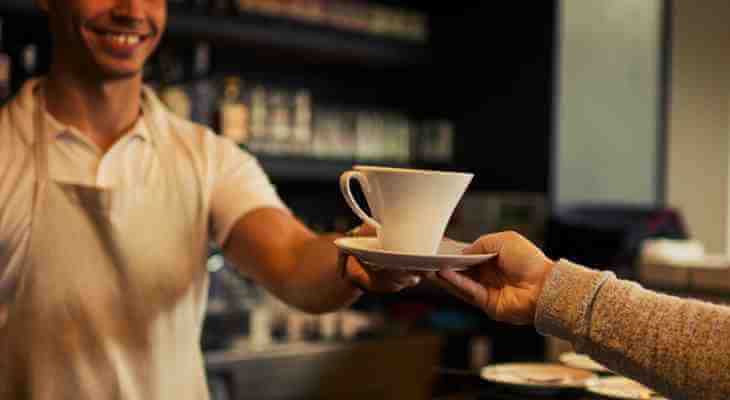 Smiling barista handing a cup of coffee to a customer.