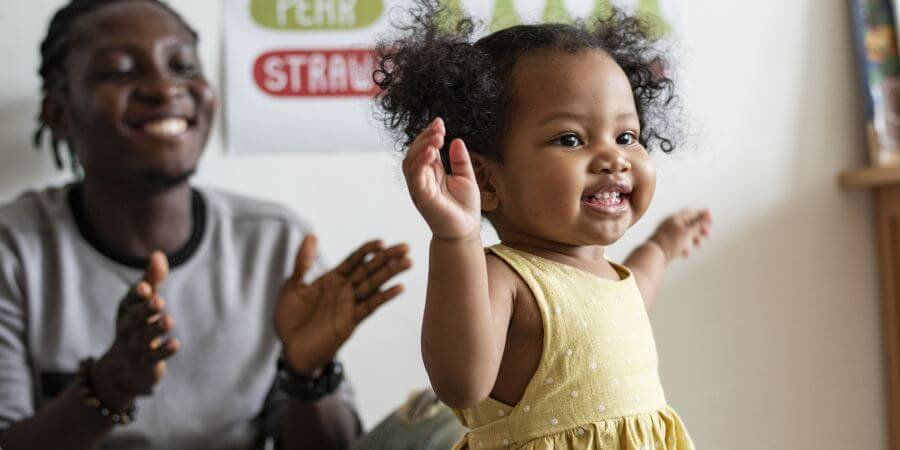 A toddler dancing with her parent watching on.