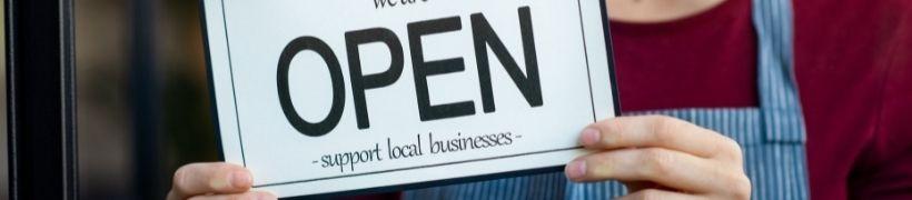 Person holding a sign saying 'open - support local businesses'